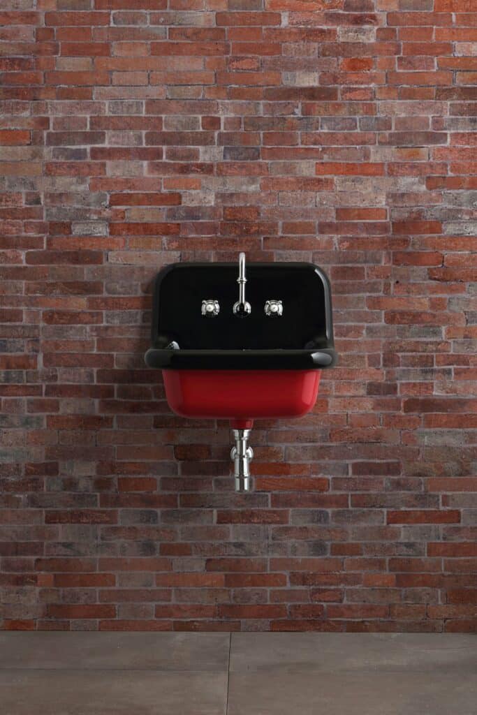 Lavabo sospeso bicolore con interno Nero Lucido ed esterno Rosso, davanti a un muro di mattoni